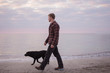 morning walk of the young man and black labrador dog on the beach